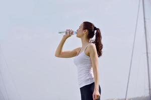 Young beautiful woman drinking water after fitness exercise photo