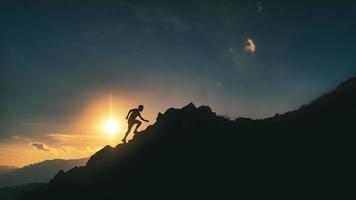 el hombre sube una montaña rocosa en una pintoresca puesta de sol foto