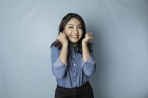 A portrait of a cute Asian woman wearing a blue shirt and feeling excited and isolated by a blue background photo