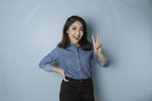 mujer asiática emocionada con una camisa azul dando el número 12345 con un gesto manual foto