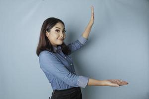 mujer asiática emocionada con pantalones azul apuntando al espacio de copia a su lado, aislada por fondo azul foto