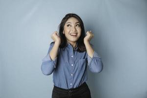 A portrait of a cute Asian woman wearing a blue shirt and feeling excited and isolated by a blue background photo