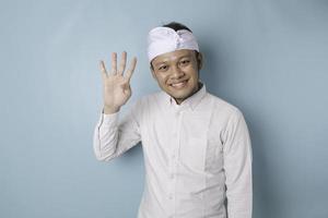 Excited Balinese man wearing udeng or traditional headband and white shirt giving number 12345 by hand gesture photo