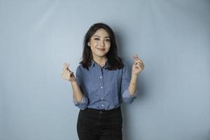 An attractive young Asian woman wearing a blue shirt feels happy and a romantic shapes heart gesture expresses tender feelings photo