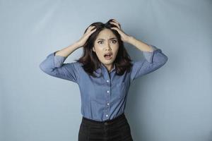 Portrait of young Asian woman isolated by blue background feeling frustrated with helpless face expression. photo