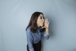 joven mujer hermosa con una camisa azul gritando y gritando fuerte a un lado con una mano en la boca. concepto de comunicación foto