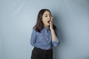 Portrait of sleepy attractive Asian woman wearing a blue shirt, feeling tired after night without sleep, yawning photo