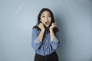 A portrait of a cute Asian woman wearing a blue shirt and feeling excited and isolated by a blue background photo