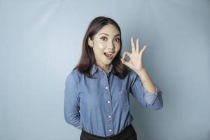 mujer asiática emocionada con una camisa azul dando un gesto de mano bien aislado por un fondo azul foto
