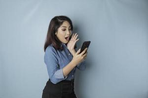 sorprendida mujer asiática con pantalones azul apuntando a su smartphone, aislada de fondo azul foto