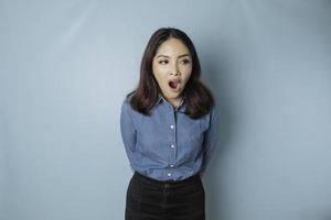 Portrait of sleepy attractive Asian woman wearing a blue shirt, feeling tired after night without sleep, yawning photo