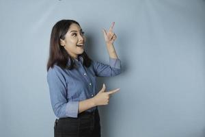 mujer asiática emocionada con pantalones azul apuntando al espacio de copia a su lado, aislada por fondo azul foto