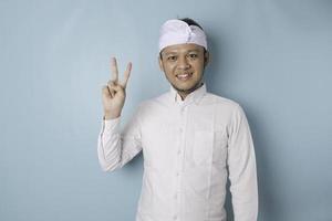 Excited Balinese man wearing udeng or traditional headband and white shirt giving number 12345 by hand gesture photo