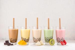 Row of fresh boba bubble tea glasses with straw on white background. Slices of fruity ingredients with delicious glasses of a summer refreshment. photo