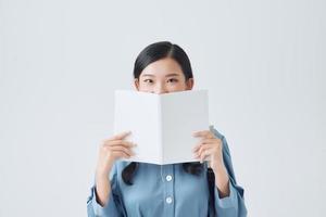 Happy pensive girl holding white notebook, covering half of face, looking attentively at camera, photo