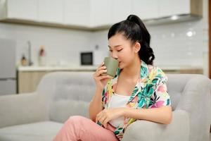 Young woman resting on couch and drinking tea in light room photo