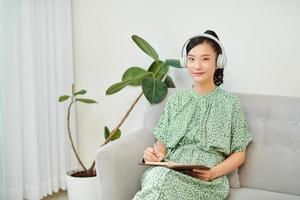 Woman listening to music and writing diary on sofa at home photo