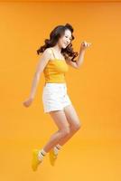 Full length portrait of a smiling pretty woman jumping isolated on a yellow background photo