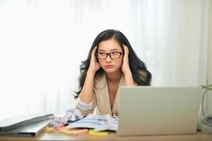 Portrait of an attractive woman at the table with cup and laptop, book, notebook on it, grabbing her head photo
