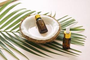 Coconut oil in bottle with open nuts and pulp in jar, green palm leaf background. Natural cosmetic products. photo
