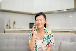 Pleasant talk with friend. Attractive smiling young redhead woman talking on cell phone while sitting on the beige sofa at home photo