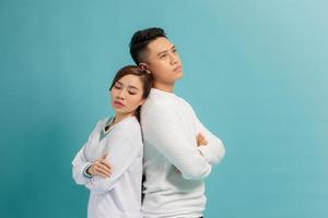 Confused young couple standing with one another's back with crossed arms over blue background photo