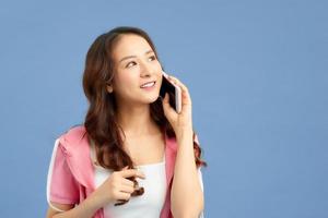 Happy young Asian woman using phone to talk with someone isolated colorful blue background. photo