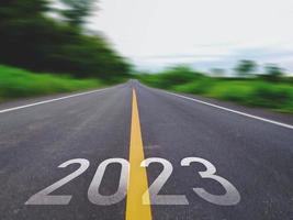 concepto de año nuevo y camino nuevo con la palabra 2022 a 2023 escrita en la carretera asfaltada en un hermoso camino rural con campos de hierba verde en ambos lados concepto para el año nuevo o visión de 2023 foto