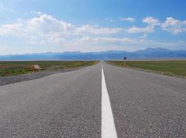 Empty road towards the horizon with mountains and clouds in the background photo