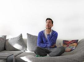 Man on couch contemplating options with a finger touching his lips photo