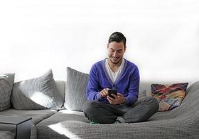 Smiling man handling smartphone while sitting on the couch photo