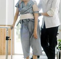 joven fisioterapeuta asiático que trabaja con un anciano usando un andador en el pasillo de un hogar de ancianos