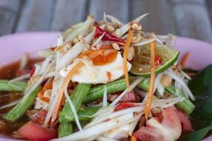 ensalada de papaya y huevo salado en plato rosa, los tailandeses llaman som tam thai kai khem. foto