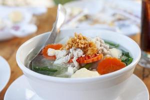 Clear Soup with Tofu and Minced Pork Thai people call Kang Jued Tao Hoo in a white bowl with spoon on dining table. photo