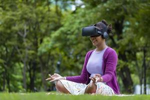 mujer afroamericana practicando relajantemente la meditación en el bosque usando la realidad virtual de las gafas vr para lograr la sabiduría de la paz interior para una mente y un alma sanas en un universo de metaverso paralelo