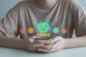 Hand holding mobile smartphone and select happy face for feedback service rating experience. Satisfaction survey with negative, neutral and positive facial expressions. Business rating experience. photo