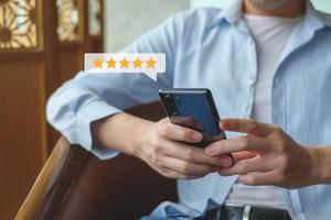 Customer hand press on smartphone screen with gold five star rating feedback icon excellent rank level for giving best score point to review the service , ranking experience, evaluate quality. photo