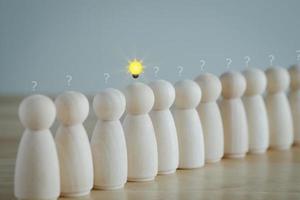 Leader with idea and innovation and creativity concept. Creative process concept and problem solution. Wooden human with  glowing light bulb among many question mark. Standing out from the crowd. photo