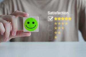 Customer service rating experience, feedback emotion and satisfaction survey with negative, neutral and positive facial expressions. hand showing smiley face icon on wood cube with 5 star. photo