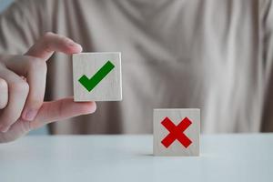 Woman hand pick correct check mark on wooden cube with cross symbol stand on table for true or false changing mindset or way of adapting to change leader and transform quiz answer and poll concept. photo