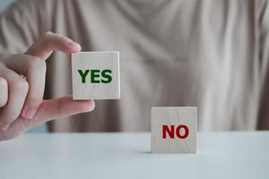 Think With Yes Or No Choice.Test question. Choice hesitate, opposition, opponent view. making decision. Woman hand showing Yes word on wood cube with No text didn't choose stand on table. photo