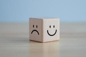 Happy face and sad face on wooden block cube for positive mindset selection, Service rating, satisfaction concept. photo