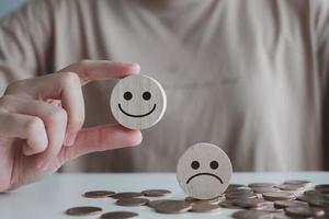 experiencia de calificación de servicios comerciales, concepto de encuesta de satisfacción. el cliente eligió a mano una cara sonriente feliz y un icono de cara triste borrosa en un círculo de madera. foto