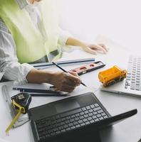 Two colleagues discussing data working and tablet, laptop with on on architectural project at construction site at desk in office photo