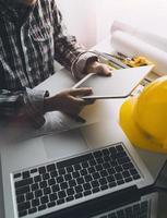 Two colleagues discussing data working and tablet, laptop with on on architectural project at construction site at desk in office photo