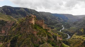 Aerial panning view dramatic landscape with historical Tmogvi fortress ruins with old wall on hilltop surrounded scenic Mtkvari river and canyon panorama video