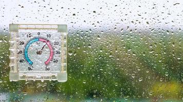 gotas de lluvia y termómetro húmedo al aire libre sobre vidrio foto