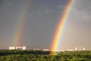 double rainbow in gray sky over sunlit city park photo