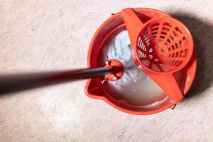 top view of mop rinsing in red bucket with water photo