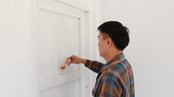 A painter is painting white with a painted plot on the door of a white wooden house. video